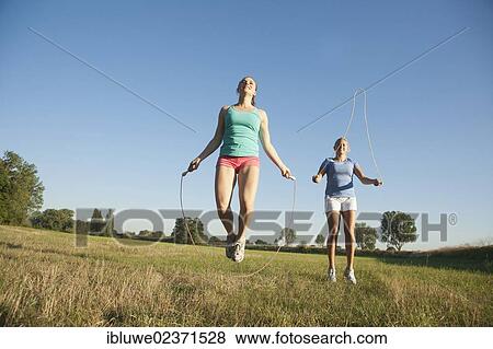 Stock Photo - Two young women jumping rope in a meadow. Fotosearch