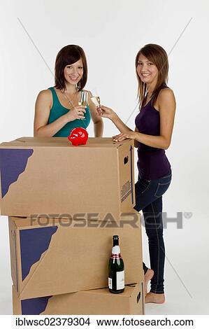 Picture - Two young women moving house clinking champagne glasses. Fotosearch