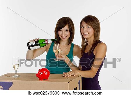 Stock Image - Two young women moving house drinking a glass of champagne. Fotosearch