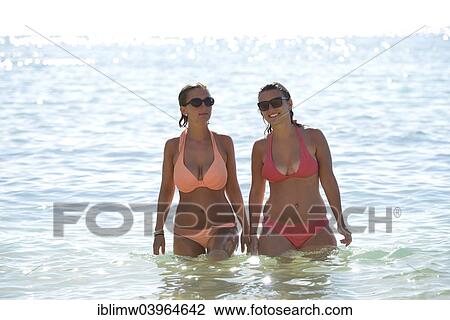 Stock Image - "Two young women wearing bikinis in the sea, Playa de Papagayo or Papagayo beach, Lanzarote, Canary Islands, Spain, Europe". Fotosearch
