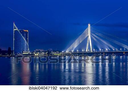 Stock Image - "Vansu Bridge, cable-stayed bridge, dusk, blue hour, over the Daugava river or Western Dvina, with the Swedbank building, Riga, Latvia, Europe". Fotosearch