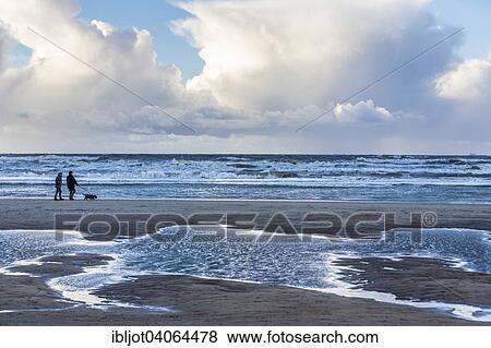 Stock Photo - "Walkers, North Sea beach, stormy sea, stormy clouds during an autumn storm, De Haan, Flanders, Belgium, Europe". Fotosearch