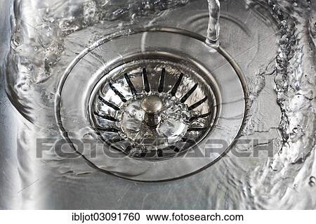 Stock Image - "Water flowing into the drain of a sink, symbolic image for water consumption, water wastage". Fotosearch
