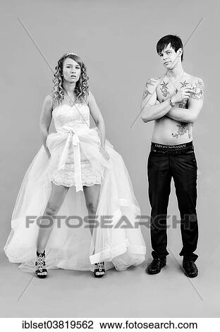 Stock Image - "Wedding picture, a bride in a short dress and a bare chested groom with tattoos, holding a cigarette". Fotosearch