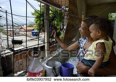 Stock Image - "Woman, 38, with her son, 1 year, looking out the window of her house in the Senador Camara favela, Rio de Janeiro, Rio de Janeiro State, Brazil, South America". Fotosearch