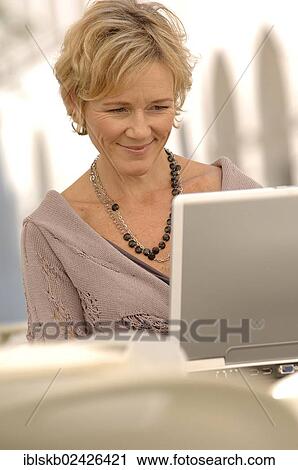 "Woman, 40-50 years, is sitting with a laptop computer at a bistro table" View Large Photo Image Stock Image - "Woman, 40-50 years, is sitting with a laptop computer at a bistro table". Fotosearch