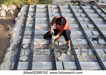 Stock Image - "Woman, 40, using a drill during the construction of a patio, Austria, Europe". Fotosearch
