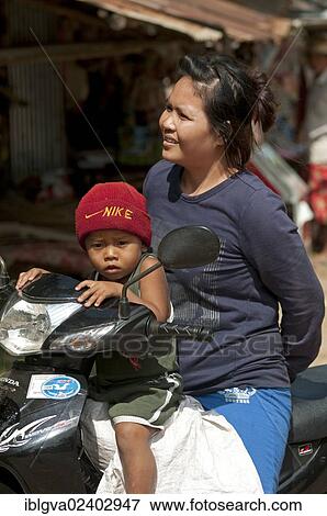 Stock Photo - "Woman and child with Nike hat on a motorcycle, Battambang, Cambodia, Southeast Asia, Asia". Fotosearch