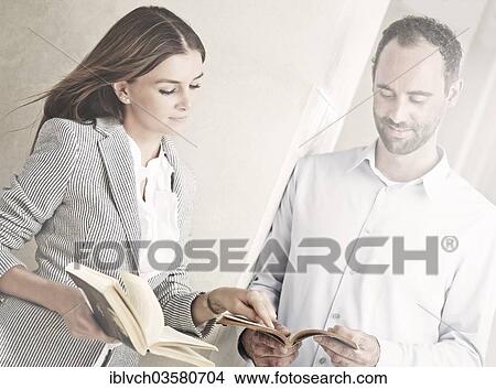 Picture - "Woman and man leaning against a wall and reading, she is showing him a section in his book, Innsbruck, Tyrol, Austria, Europe". Fotosearch
