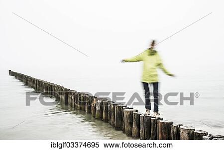 Stock Photography - "Woman balancing on groynes on the Baltic Sea coast, Zingst, Fischland-Darss-Zingst, Mecklenburg-Western Pomerania, Germany, Europe". Fotosearch