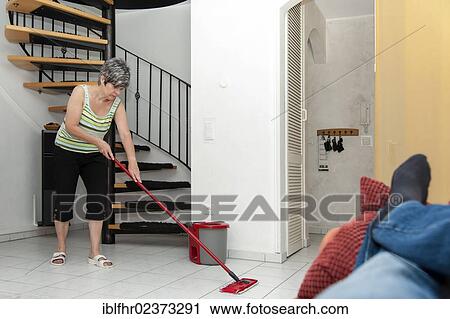 "Woman cleaning while a man is lying on the couch, Germany, Europe" View Large Photo Image Stock Image - "Woman cleaning while a man is lying on the couch, Germany, Europe". Fotosearch