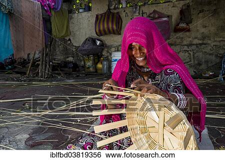 Stock Photograph - "Woman covered in a pink veil is braiding a basket on the pavement, Mahim, Mumbai, Maharashtra, India, Asia". Fotosearch