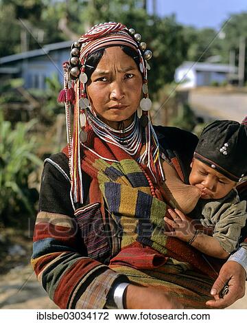 Stock Image - "Woman from the people of the Akha wearing traditional costume while nursing a boy, Tachilek, Shan State, Myanmar, Burma, Asia". Fotosearch