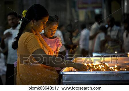 Stock Photo - "Woman holding a child in her arms while lighting oil lamps in a temple, Meenakshi Amman Temple or Sri Meenakshi Sundareswarar Temple, Madurai, Tamil Nadu, India, Asia". Fotosearch