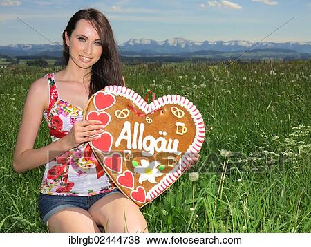 Stock Photo - Woman holding a gingerbread heart labelled with the word Allgaeu. Fotosearch