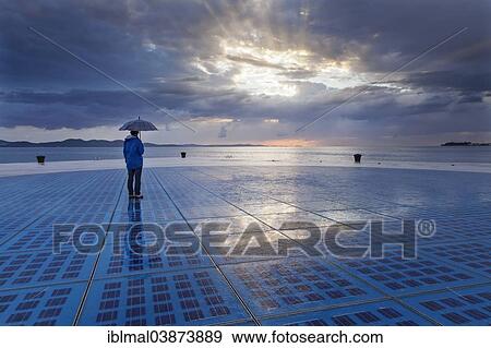 "Woman holding an umbrella, standing on the solar art installation """"Greeting to the Sun"""", Zadar, Dalmatia, Croatia, Europe" View Large Photo Image Stock Photo - "Woman holding an umbrella, standing on the solar art installation """"Greeting to the Sun"""", Zadar, Dalmatia, Croatia, Europe". Fotosearch