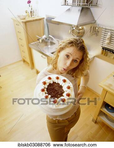 Stock Photograph - Woman in a kitchen holding a Black Forest cherry cake. Fotosearch