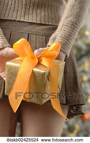"Woman in a mini skirt is holding gift wrapped in golden paper, from behind, at Christmas time" View Large Photo Image Picture - "Woman in a mini skirt is holding gift wrapped in golden paper, from behind, at Christmas time". Fotosearch