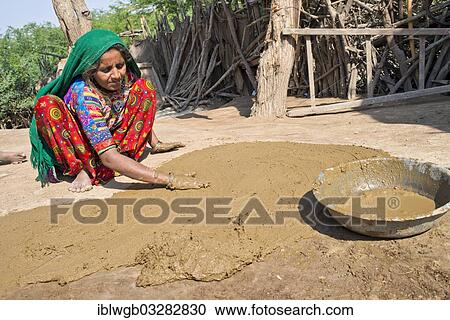 Stock Image - "Woman in traditional dress plastering the floor of a courtyard with a mixture of water, sand and cow dung, Rann of Kutch, Gujarat, India, Asia". Fotosearch