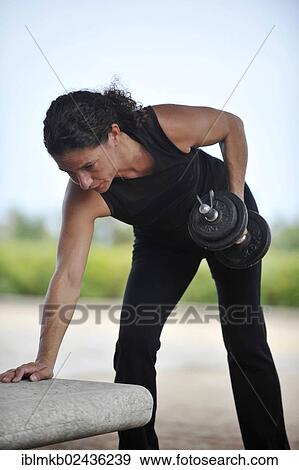 Woman lifting weights while exercising in a park View Large Photo Image Stock Photo - Woman lifting weights while exercising in a park. Fotosearch