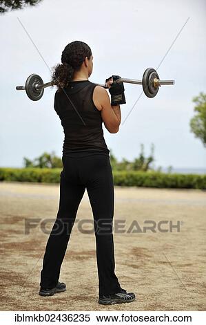 Woman lifting weights while exercising in a park View Large Photo Image Stock Photography - Woman lifting weights while exercising in a park. Fotosearch