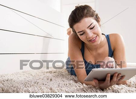 Woman lying on the floor and chatting on her tablet computer View Large Photo Image Picture - Woman lying on the floor and chatting on her tablet computer. Fotosearch