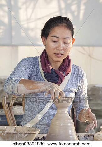 Stock Image - "Woman molding a piece of pottery on a wheel head, Cambodia, Asia". Fotosearch
