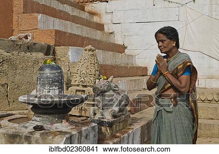 Stock Image - "Woman praying to a Shiva Lingam, at the ghats of Varanasi, India, Asia". Fotosearch
