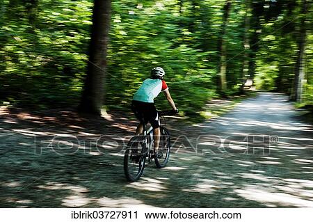Stock Image - "Woman riding a mountain bike along the Forstweg trail in Feldafinger Park, Feldafing, Upper Bavaria, Bavaria, Germany, Europe". Fotosearch