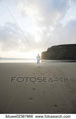Stock Photograph - Woman running along a beach at sunset. Fotosearch