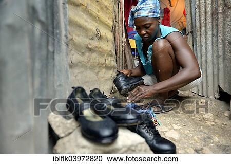 Stock Image - "Woman shining the shoes of her children for their first day of school, Camp Icare for earthquake refugees, Fort National, Port-au-Prince, Haiti, North America". Fotosearch