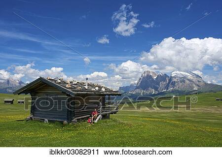 "Woman sitting at an alpine hut in front of Piatto Mountain and Sasso Lungo Mountains, Seiser Alm, Dolomiten, South Tyrol province, Trentino-Alto Adige, Italy, Europe" View Large Photo Image Stock Image - "Woman sitting at an alpine hut in front of Piatto Mountain and Sasso Lungo Mountains, Seiser Alm, Dolomiten, South Tyrol province, Trentino-Alto Adige, Italy, Europe". Fotosearch