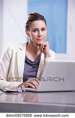 Stock Photo - "Woman sitting at desk with laptop, Munich, Upper Bavaria, Bavaria, Germany, Europe". Fotosearch