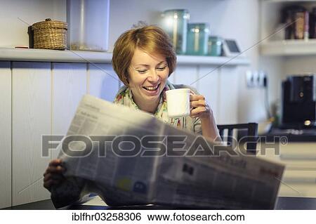 Stock Photograph - "Woman sitting at the kitchen table reading the newspaper, laughing, Germany, Europe". Fotosearch
