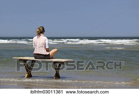 "Woman sitting cross-legged on a wooden table on a seaside beach and looking at the waves, rear view, Nordsee, Spiekeroog, Lower Saxony, Germany, Europe" View Large Photo Image Stock Image - "Woman sitting cross-legged on a wooden table on a seaside beach and looking at the waves, rear view, Nordsee, Spiekeroog, Lower Saxony, Germany, Europe". Fotosearch