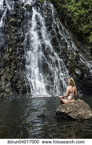 Stock Image - "Woman sitting in front of the Kepirohi waterfall, Pohnpei, Micronesia, Oceania". Fotosearch