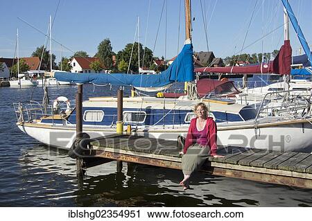 Stock Image - "Woman sitting on a jetty at the Eldena marina, Greifswald, Mecklenburg-Western Pomerania, Germany, Europe". Fotosearch