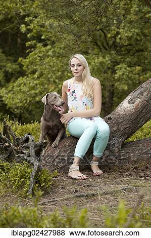 Woman sitting with a Labrador Retriever on a tree trunk View Large Photo Image Stock Photo - Woman sitting with a Labrador Retriever on a tree trunk. Fotosearch