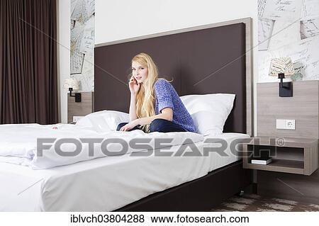 Stock Photo - Woman sitting with her laptop on the bed in a hotel room. Fotosearch