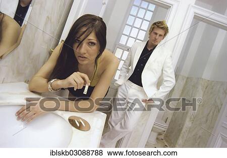 Stock Photo - "Woman snorting cocaine with a rolled bill, being watched by a man wearing a white suit and leaning on a wall". Fotosearch