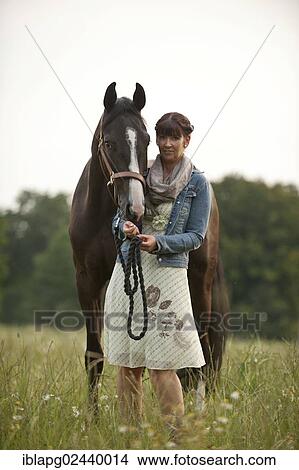 Woman standing beside a Hanoverian horse in a meadow View Large Photo Image Picture - Woman standing beside a Hanoverian horse in a meadow. Fotosearch