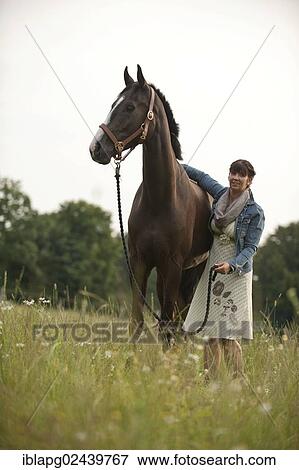 Woman standing beside a Hanoverian horse in a meadow View Large Photo Image Stock Photo - Woman standing beside a Hanoverian horse in a meadow. Fotosearch