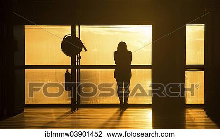 Stock Image - "Woman standing by a window watching the sunrise, atmospheric mood, Airport of Santa Cruz de La Palma, La Palma, Canary Islands, Spain, Europe". Fotosearch