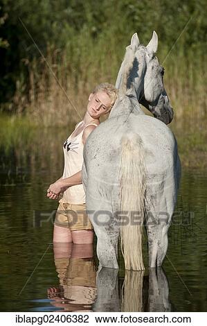 Stock Image - Woman standing in water with a Hanoverian horse. Fotosearch