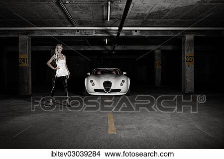 Picture - Woman standing next to a white sports car. Fotosearch