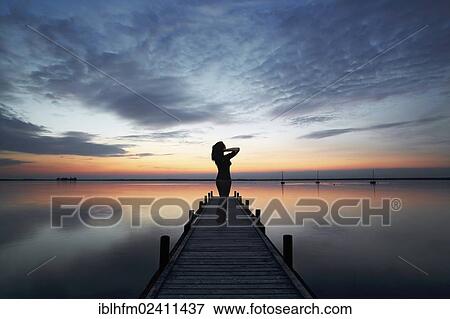 "Woman standing on a wooden dock at a lake, admiring clouds in the evening sky, Steinhude am Meer, Lower Saxony, Germany, Europe" View Large Photo Image Stock Photo - "Woman standing on a wooden dock at a lake, admiring clouds in the evening sky, Steinhude am Meer, Lower Saxony, Germany, Europe". Fotosearch