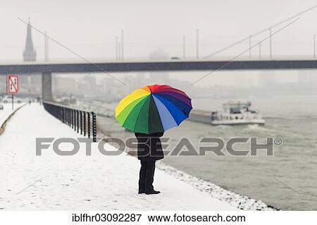 Stock Photo - "Woman standing with a colourful umbrella in winter on the bank of the Rhine River, Dusseldorf, Rhineland, North Rhine-Westphalia, Germany, Europe". Fotosearch