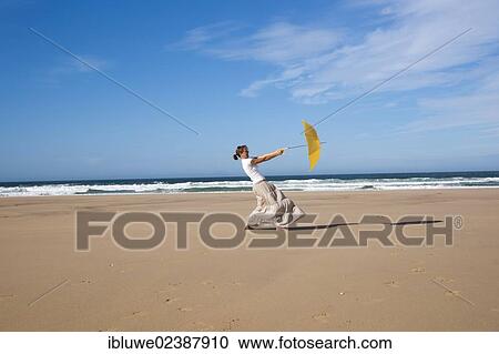 Woman walking with an umbrella on a windy beach View Large Photo Image Stock Image - Woman walking with an umbrella on a windy beach. Fotosearch