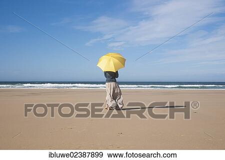 Stock Photo - Woman walking with an umbrella on a beach. Fotosearch