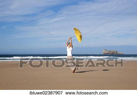 Woman walking with an umbrella on a windy beach View Large Photo Image Stock Photo - Woman walking with an umbrella on a windy beach. Fotosearch
